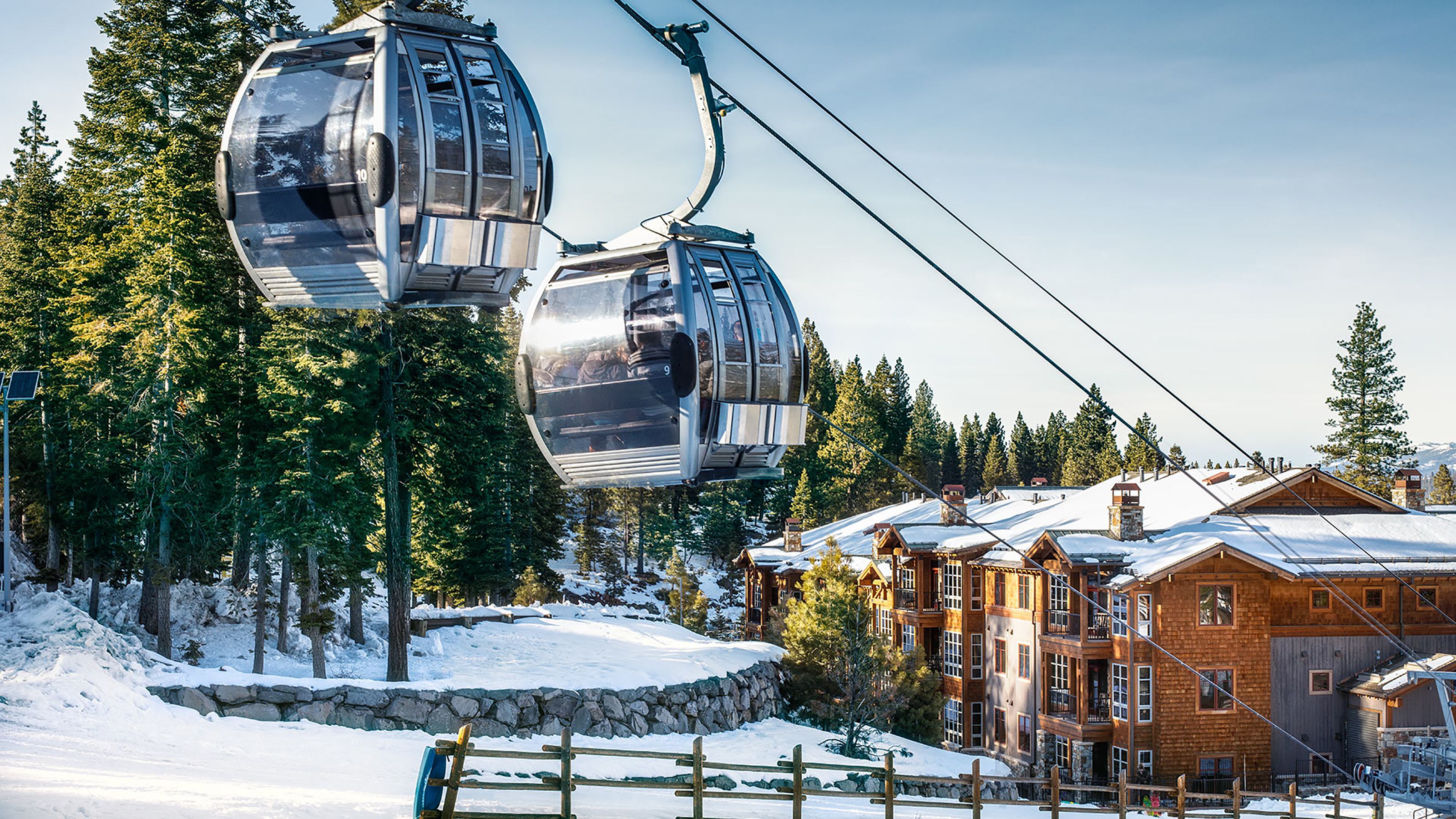 Un telesilla con cabinas, un edificio de madera con base de piedra y árboles cubiertos de nieve.