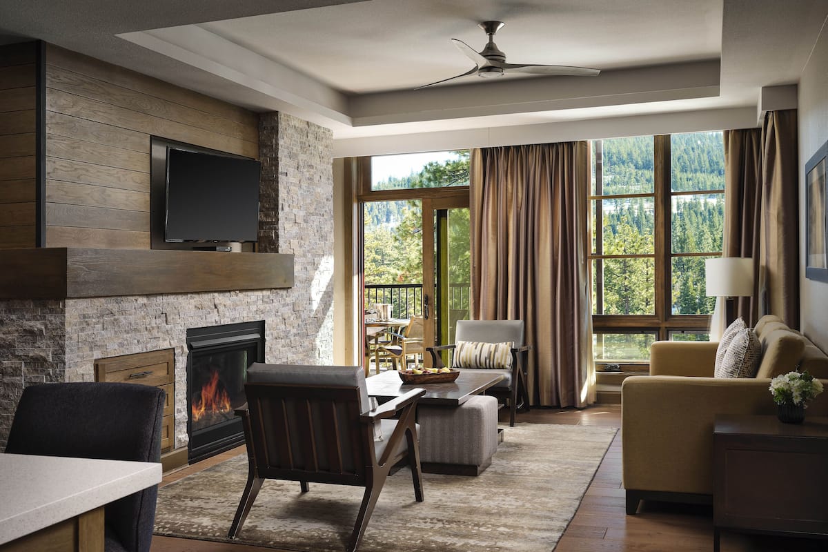 A spacious living room with a fireplace, a ceiling fan, and a large window offering a view of the outdoors.