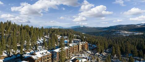 A snow-covered lodge with multiple buildings, surrounded by dense forests and mountains in the background.