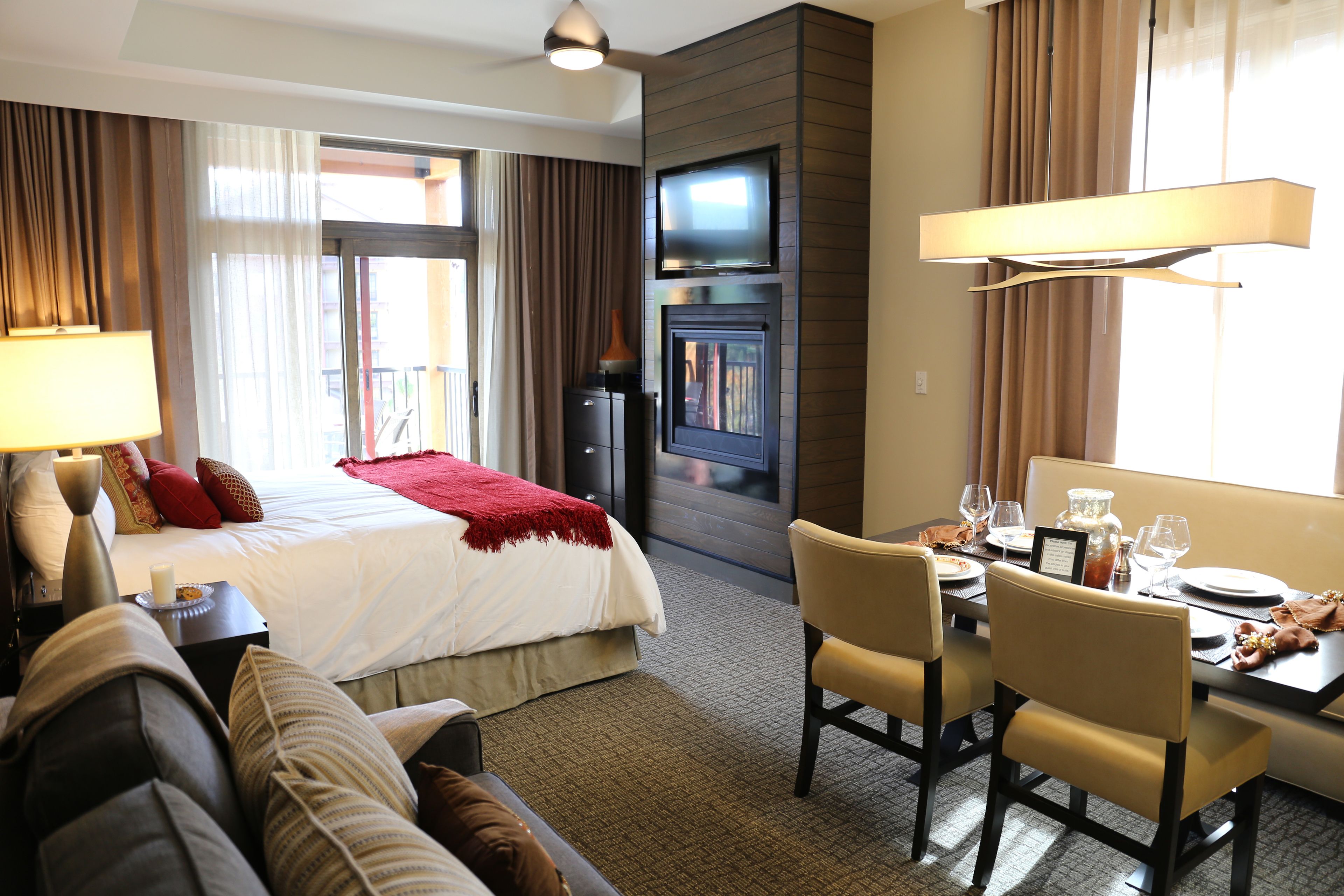 Ein Hotelzimmer mit einem Bett, einem Essbereich mit Stühlen und einem Tisch, einem an der Wand montierten Fernseher und einem Kamin.