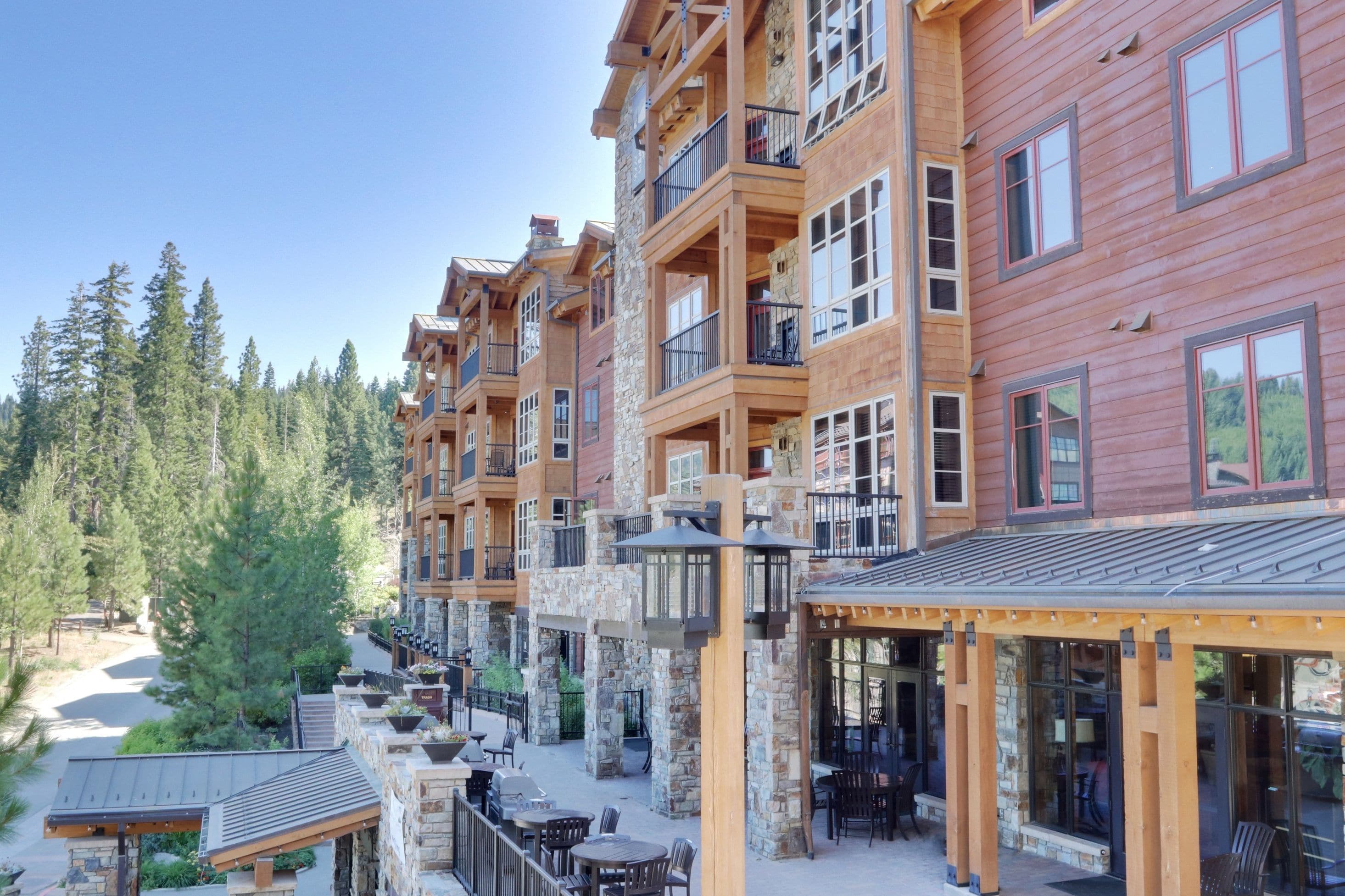 A multi-story hotel with balconies, outdoor seating, and a view of the surrounding forest.