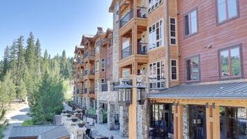A multi-story hotel with balconies, outdoor seating, and a view of the surrounding forest.