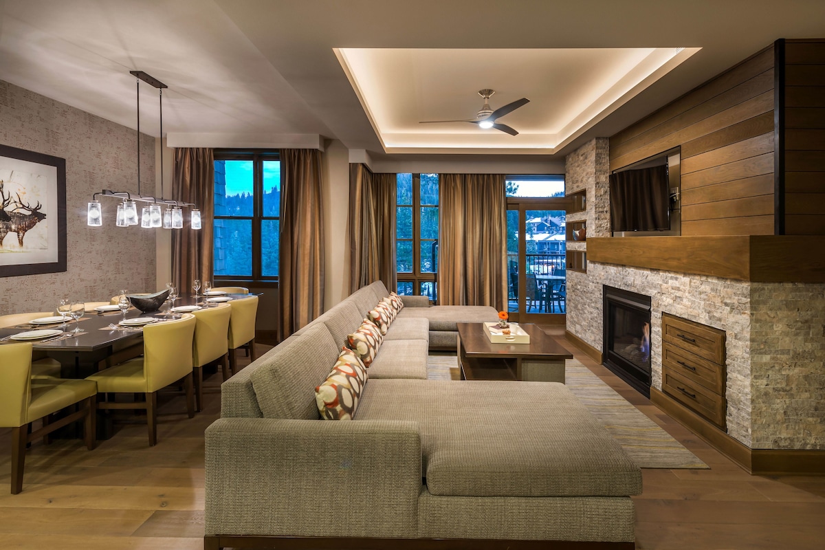 A modern living room with a sectional sofa, dining area, fireplace, and large windows.
