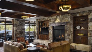 A cozy living room with stone walls, a fireplace, leather sofas, and a dining area with outdoor seating. - Hyatt Vacation Club at Northstar Lodge, Lake Tahoe (Truckee)