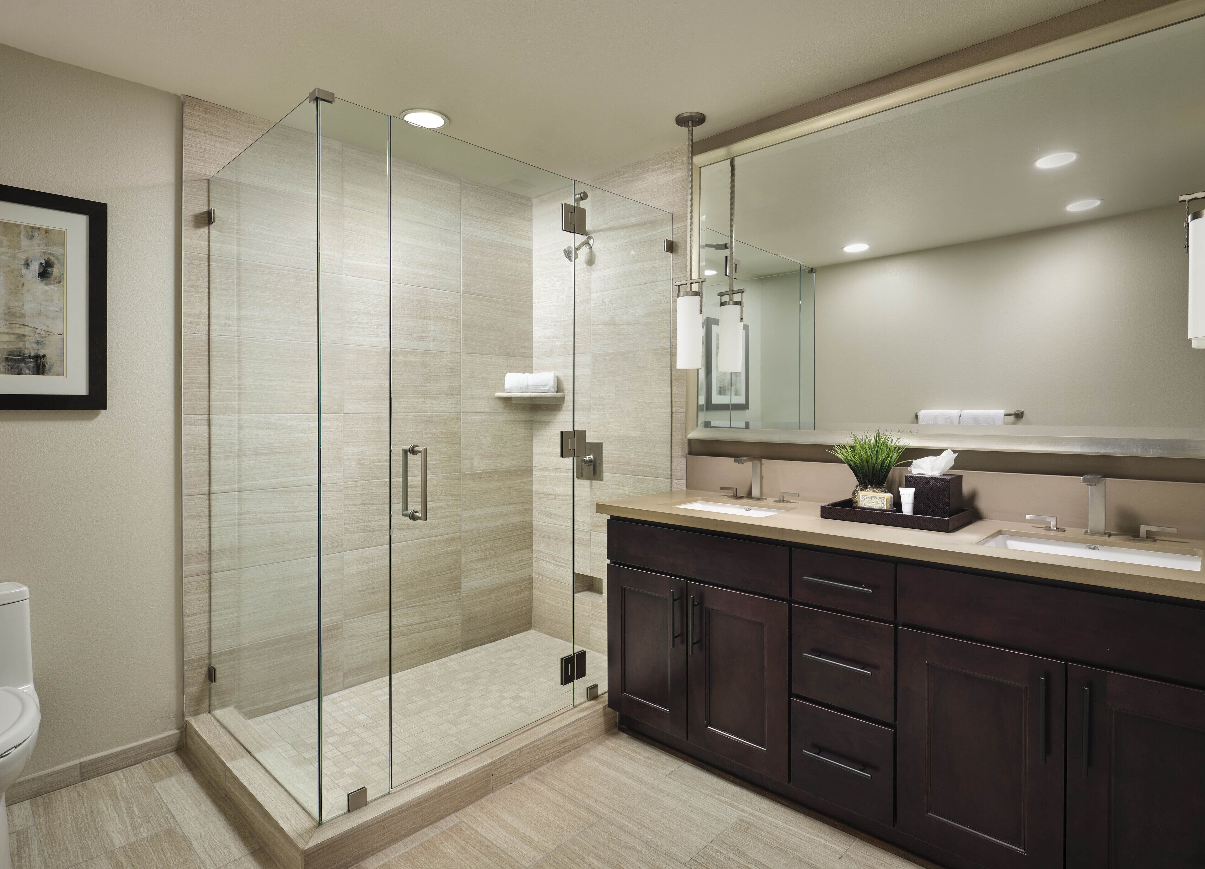 Un baño moderno con ducha envuelta en vidrio, armarios de madera oscura y un espejo grande.