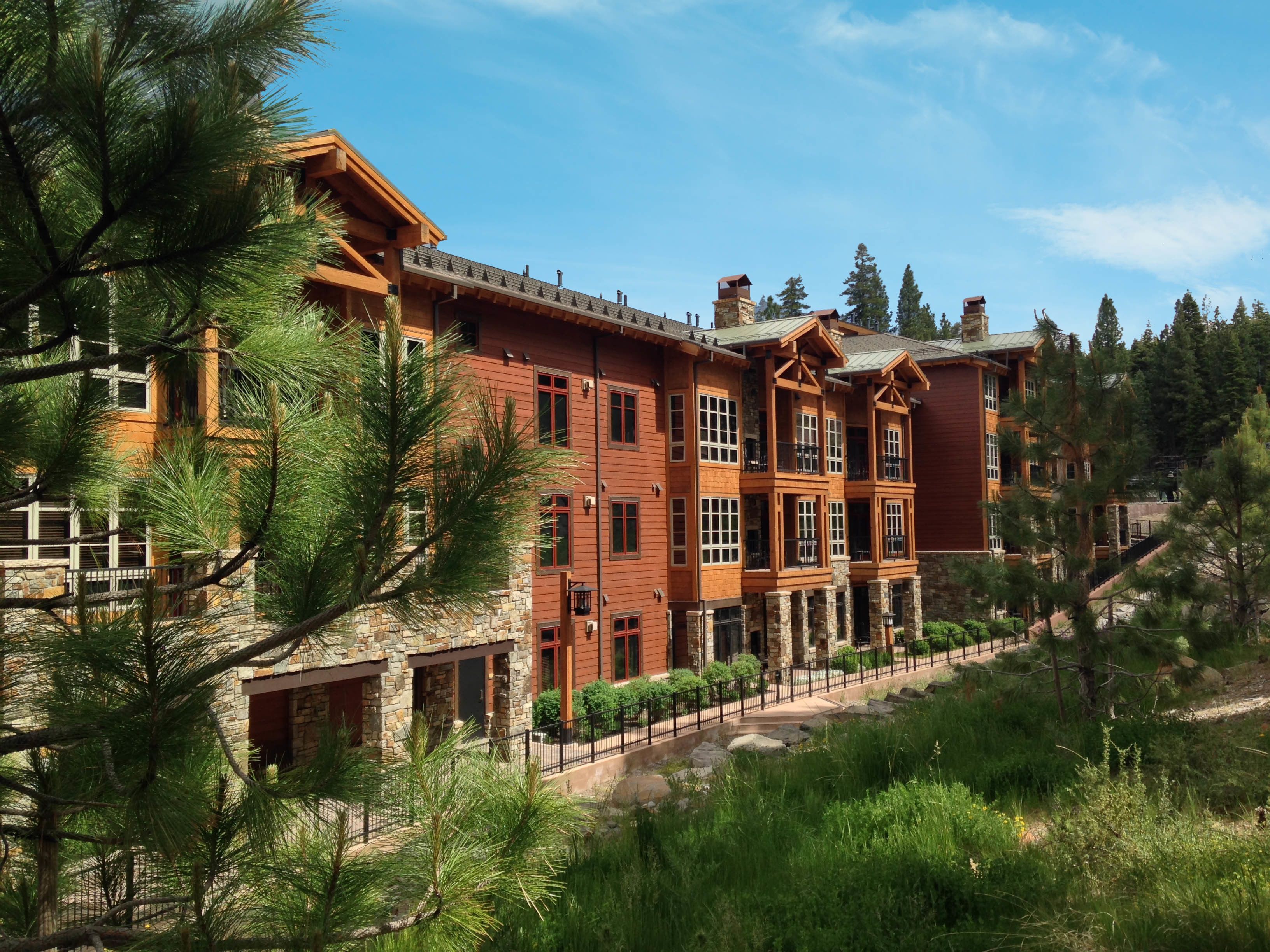 A large, multi-story building with a stone facade and wooden accents, surrounded by pine trees.
