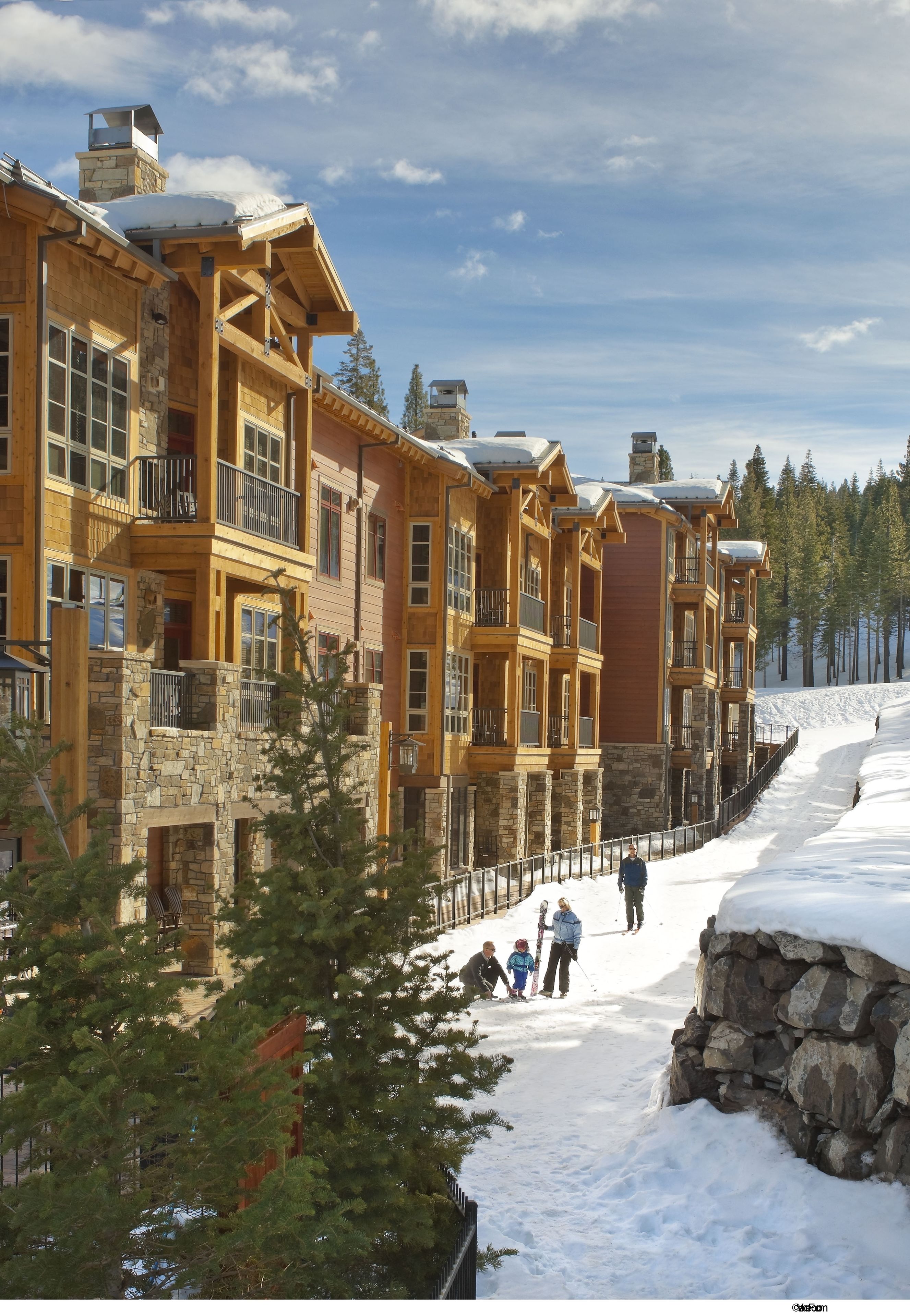 A multi-story lodge with stone and wood construction, featuring balconies and a snow-covered landscape.