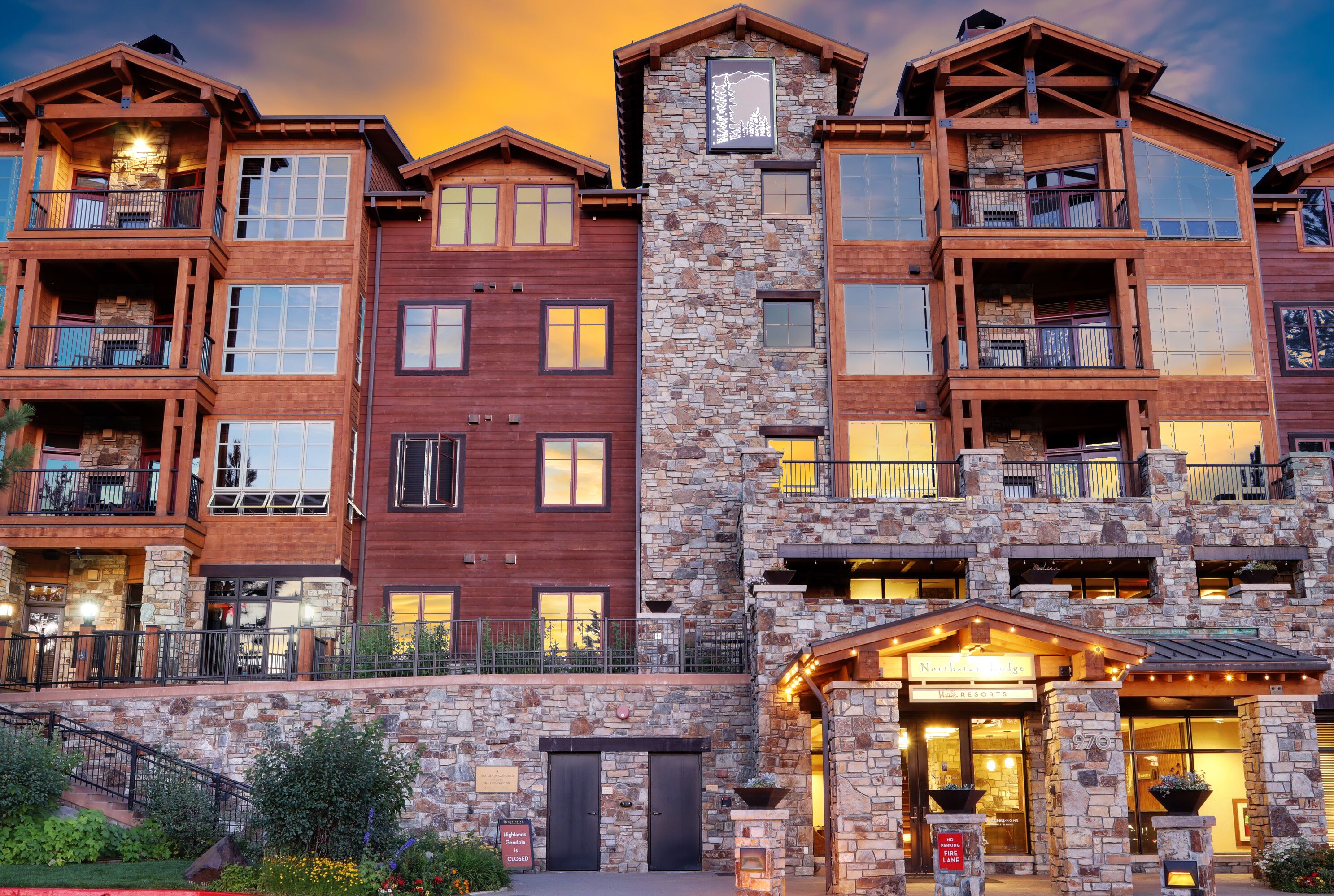 A multi-story hotel with stone and wood exterior, balconies, and a well-lit entrance.