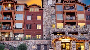 Un hotel de varios pisos con fachada de piedra y madera, balcones y una entrada bien iluminada.