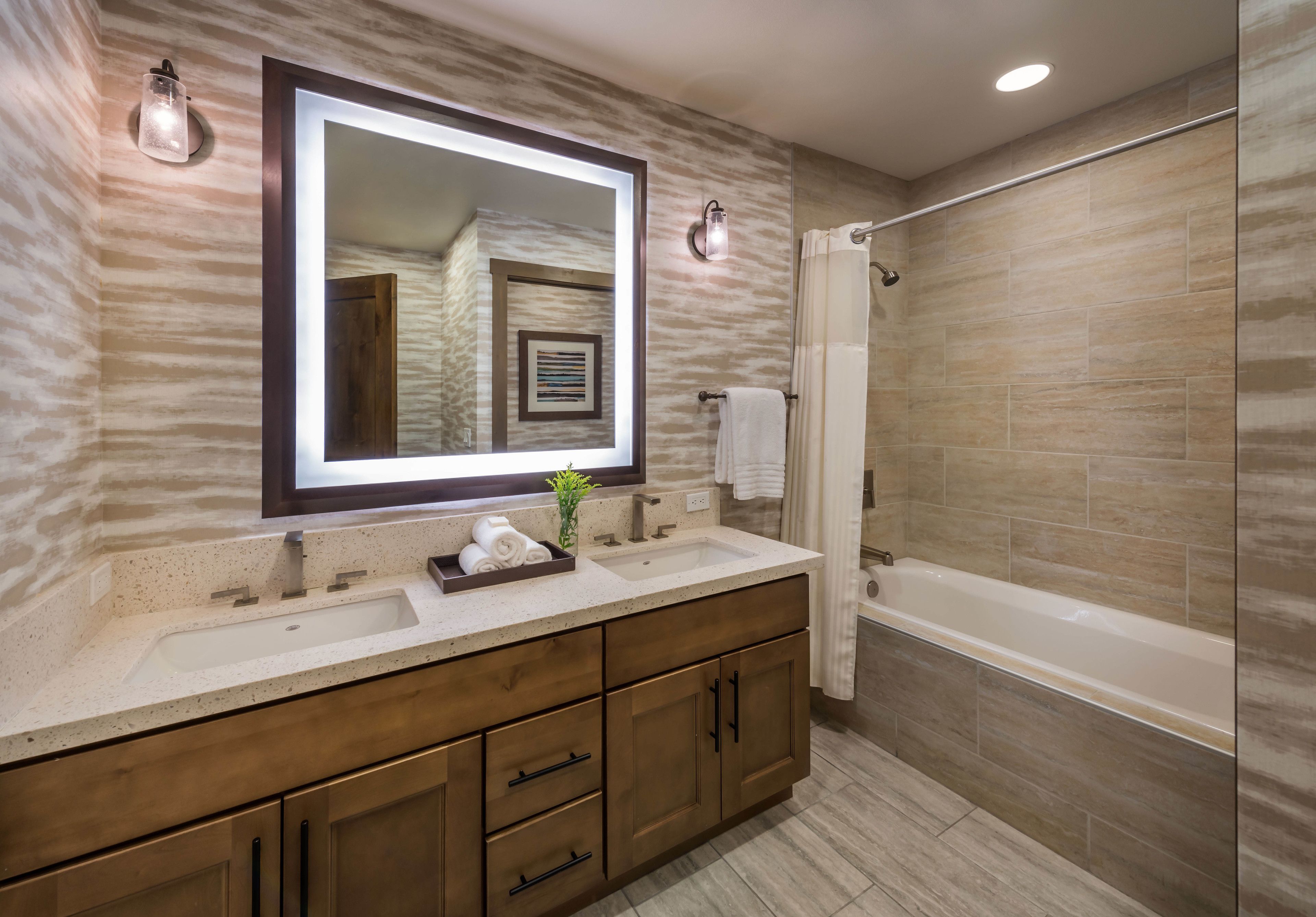 A modern bathroom with a large mirror, a sink, a bathtub, and wooden cabinetry.