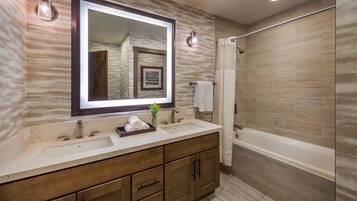 A modern bathroom with a large mirror, a sink, a bathtub, and wooden cabinetry.