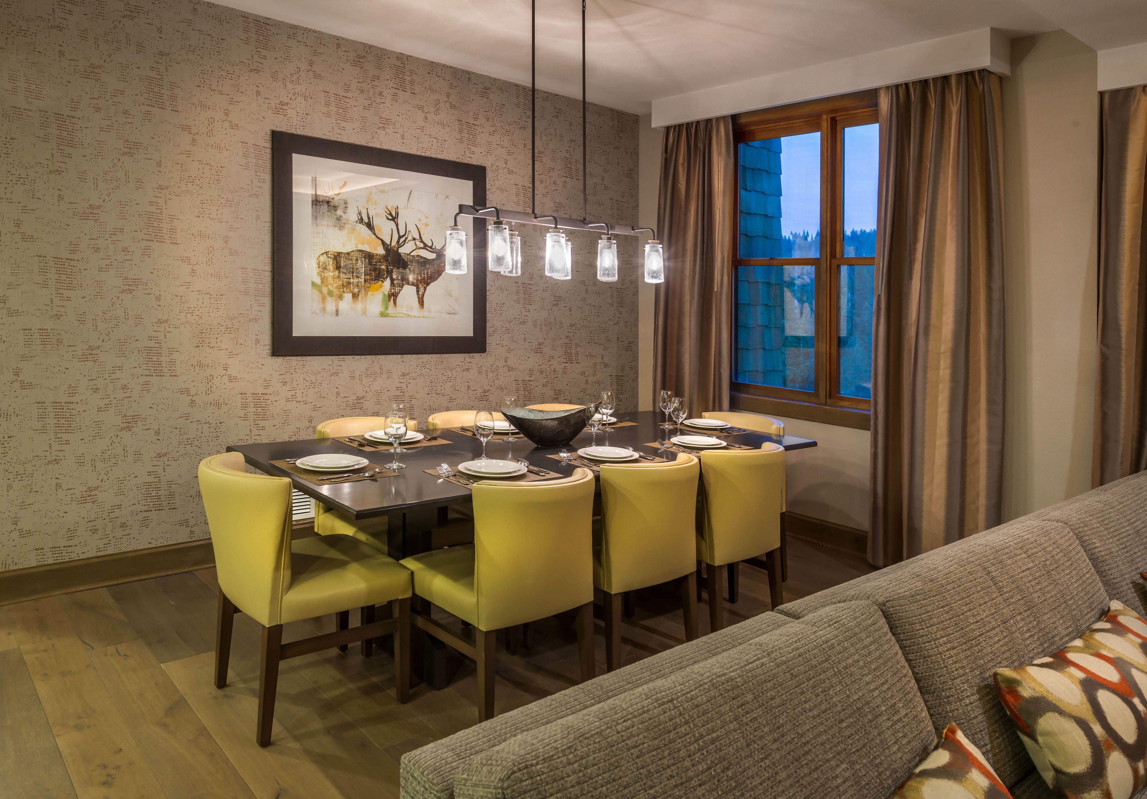 A dining area with a table set for six, yellow chairs, a framed artwork above the table, and a window with curtains.