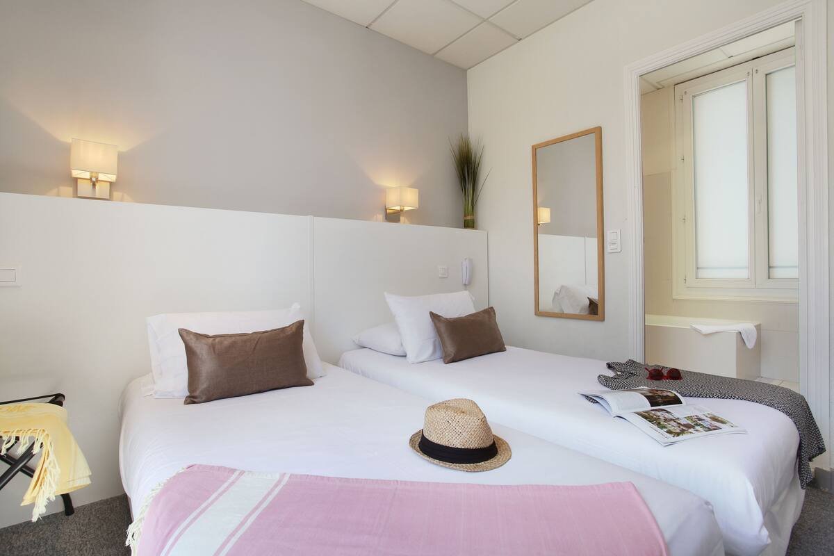 Ein Hotelzimmer mit zwei Betten, einem Spiegel, einem Fenster und einer Tür.
