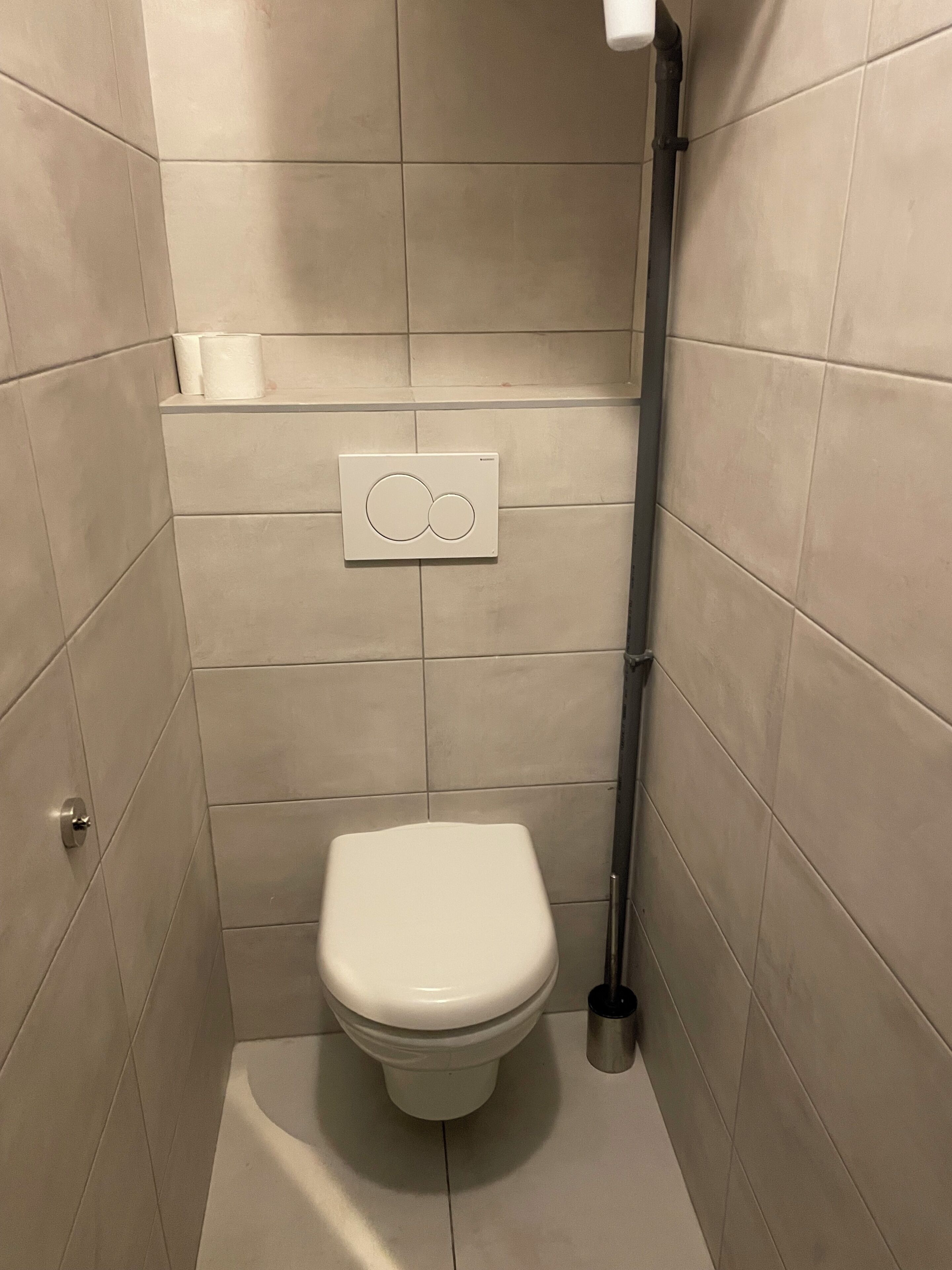 A small, modern bathroom with a toilet, a hand dryer, and a wall-mounted flush handle.