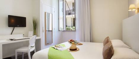 Une chambre d’hôtel équipée d’un lit, d’un bureau, d’une chaise, d’une télévision et d’une fenêtre avec des rideaux.