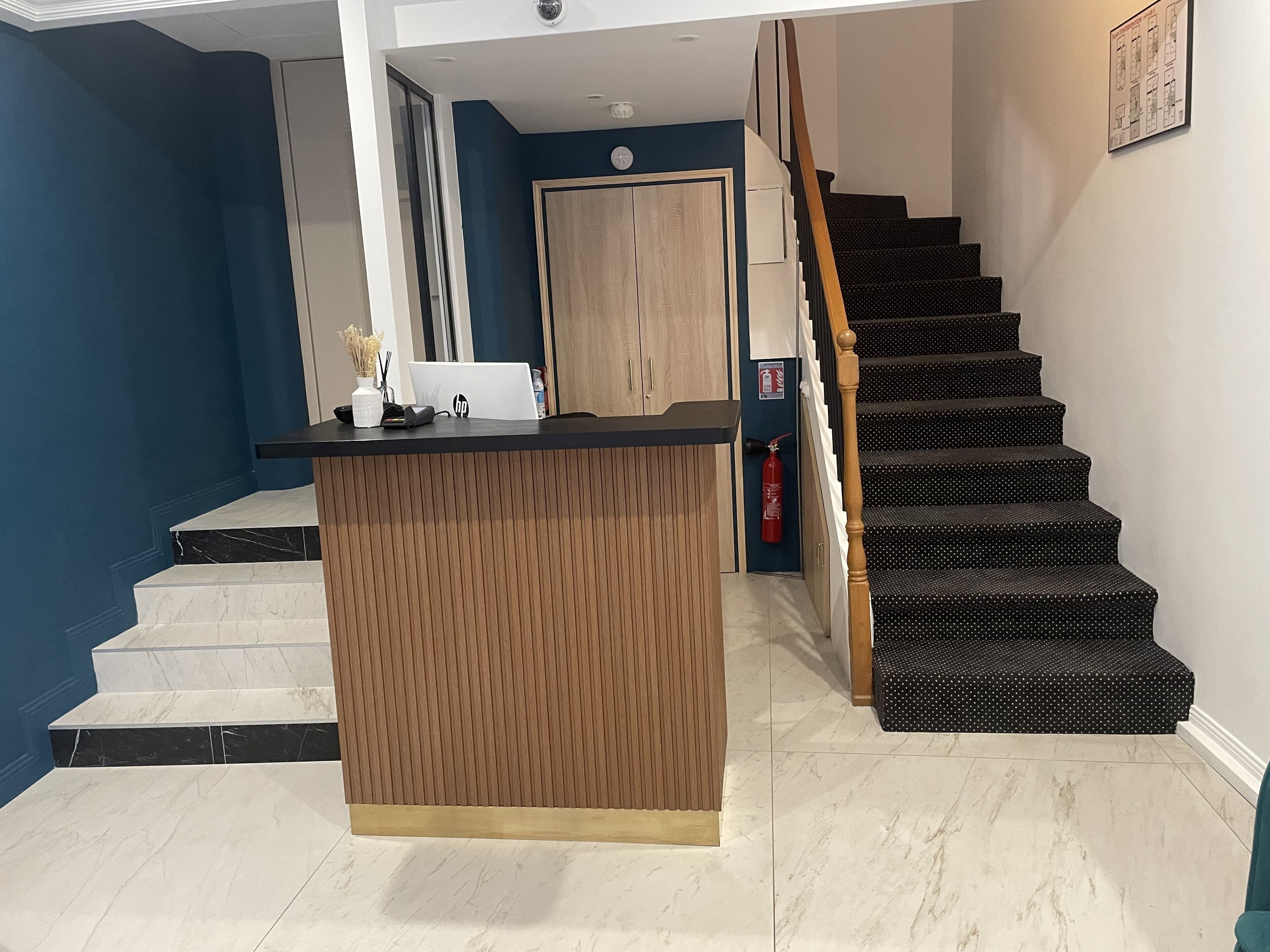 A reception desk with a laptop, a fire extinguisher, and a staircase with a polka dot carpet.