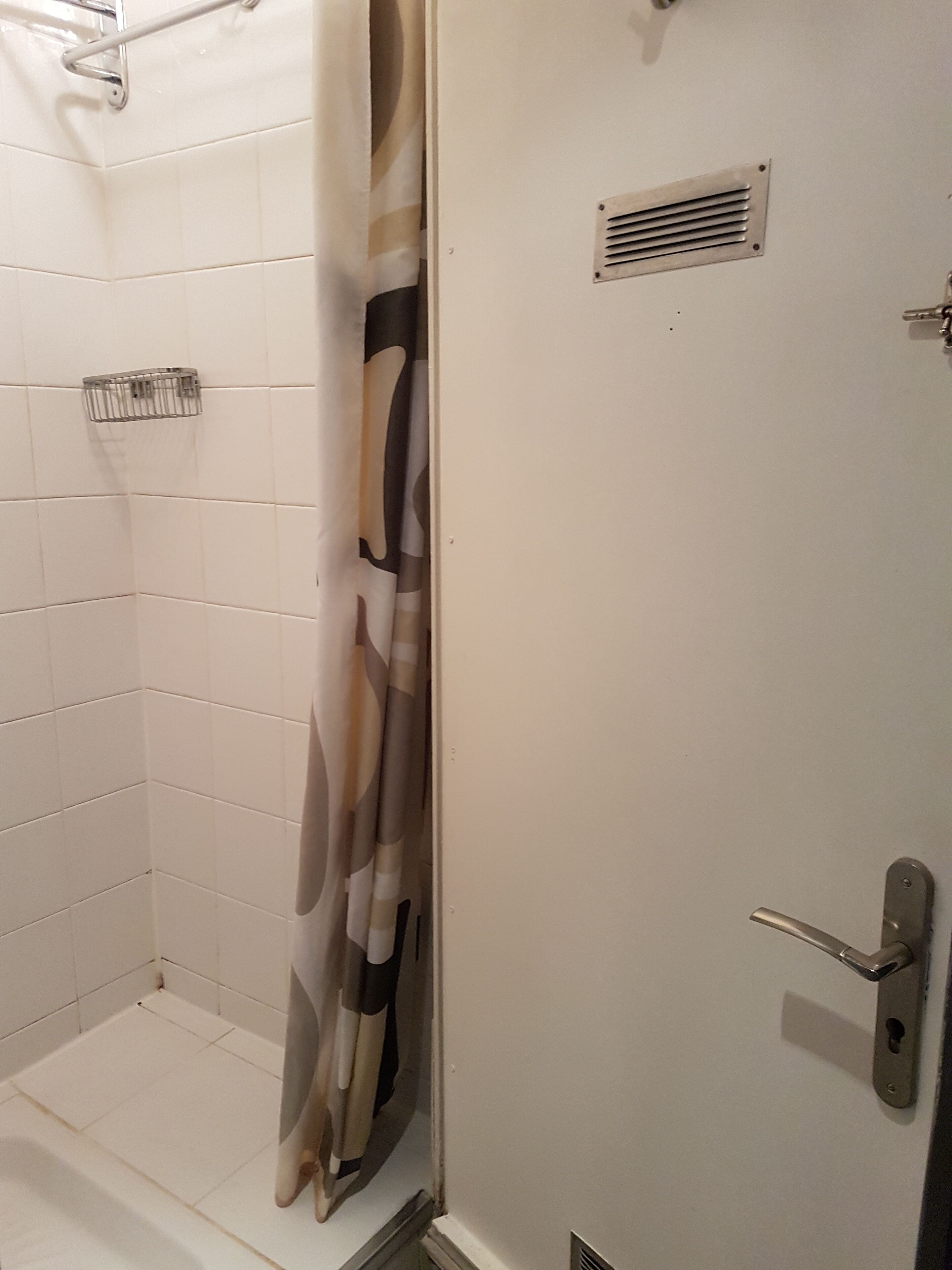 Een badkamer met witte betegelde wanden, een douchegedeelte, een handdoekhouder en een deur met een handvat.