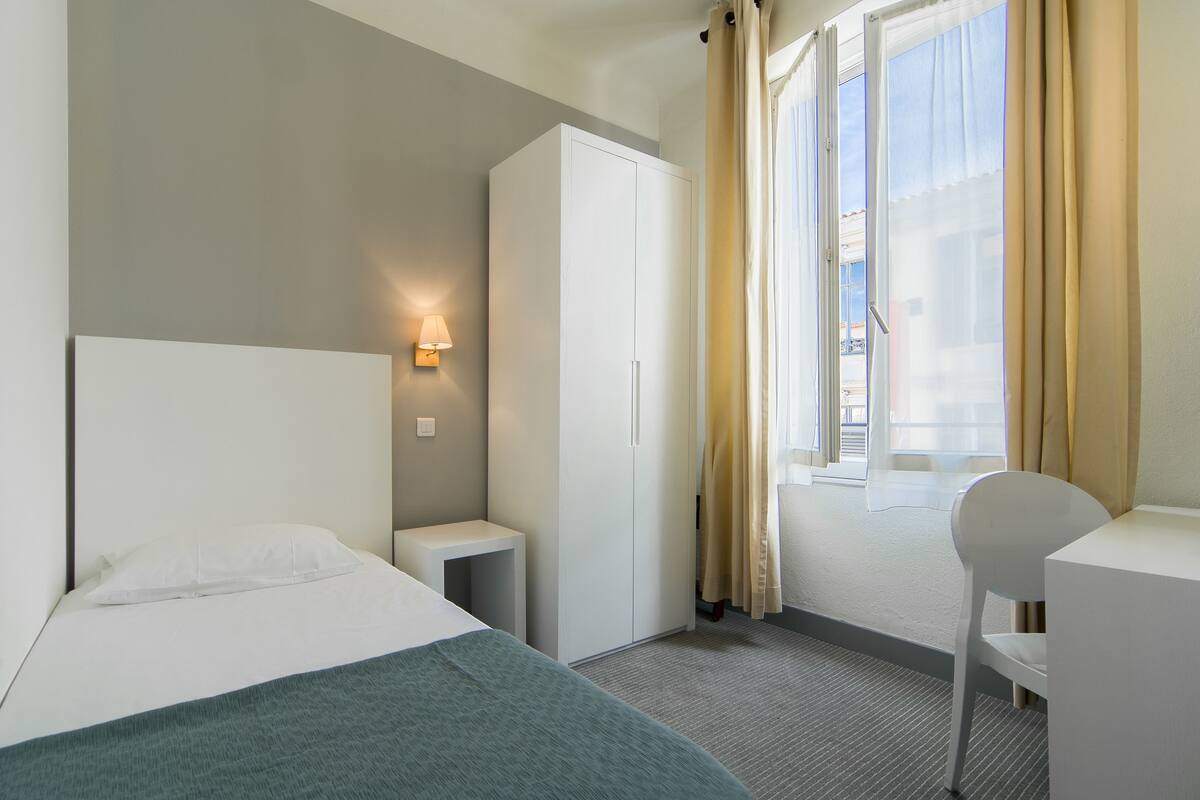 Ein Hotelzimmer mit Bett, Schreibtisch, Kleiderschrank und einem Fenster mit Vorhängen.