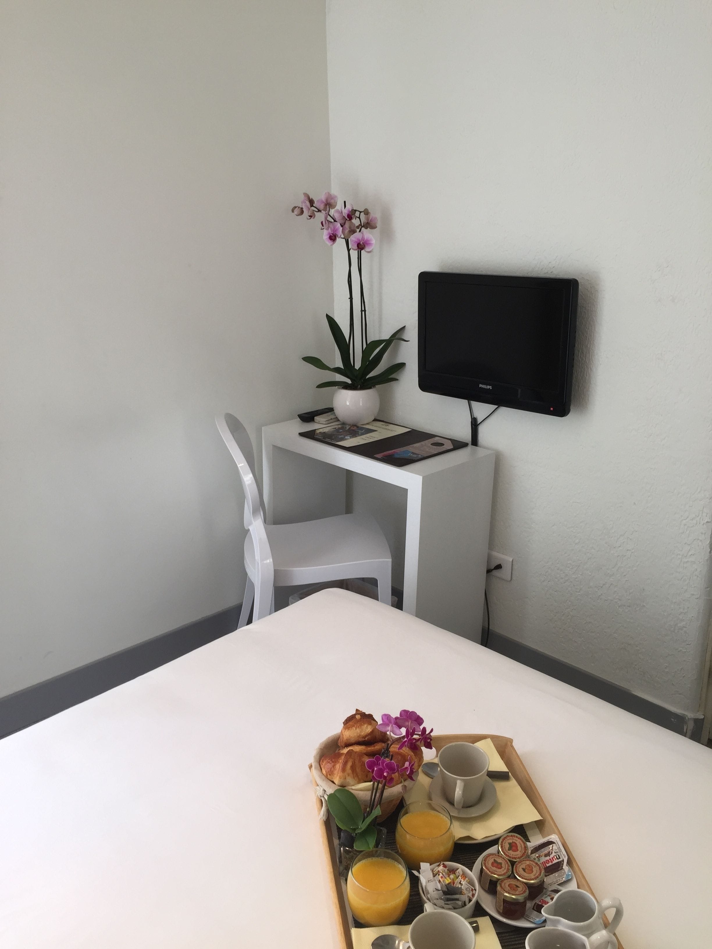 A hotel room with a bed, a desk with a chair, a TV, and a tray with breakfast items.