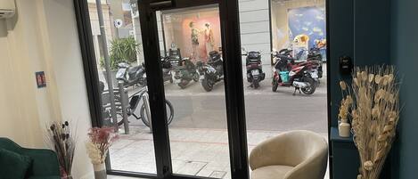 A hotel reception area with a clear view of parked motorcycles outside, a reception desk, and a doormat with "HOTEL PLM" text.
