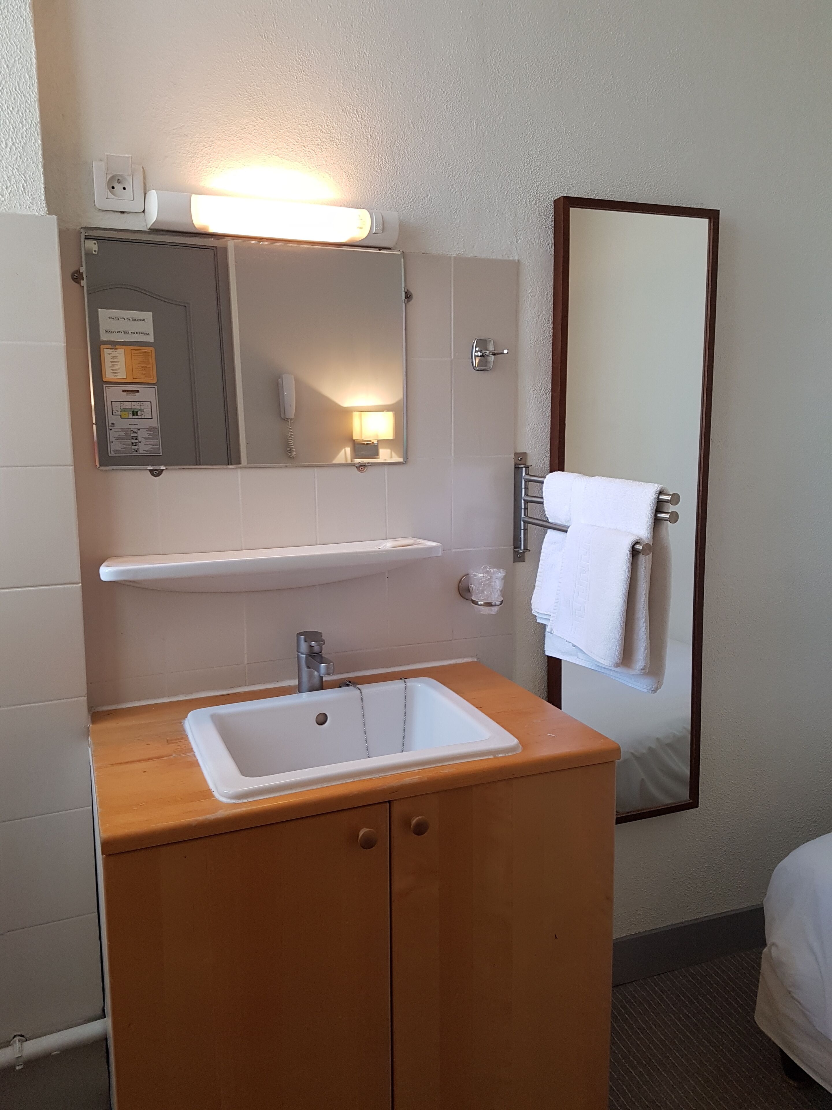 Een badkamer met een witte wastafel, een spiegel, een handdoekrek en een aan de muur bevestigde telefoon.