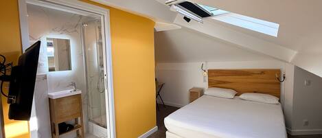 A bedroom with a bed, a wooden headboard, a small bedside table, a mirror, and a shower area.