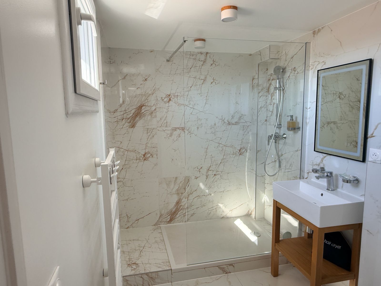 A modern bathroom with a glass shower enclosure, a white sink with a wooden vanity, and a marble backsplash.