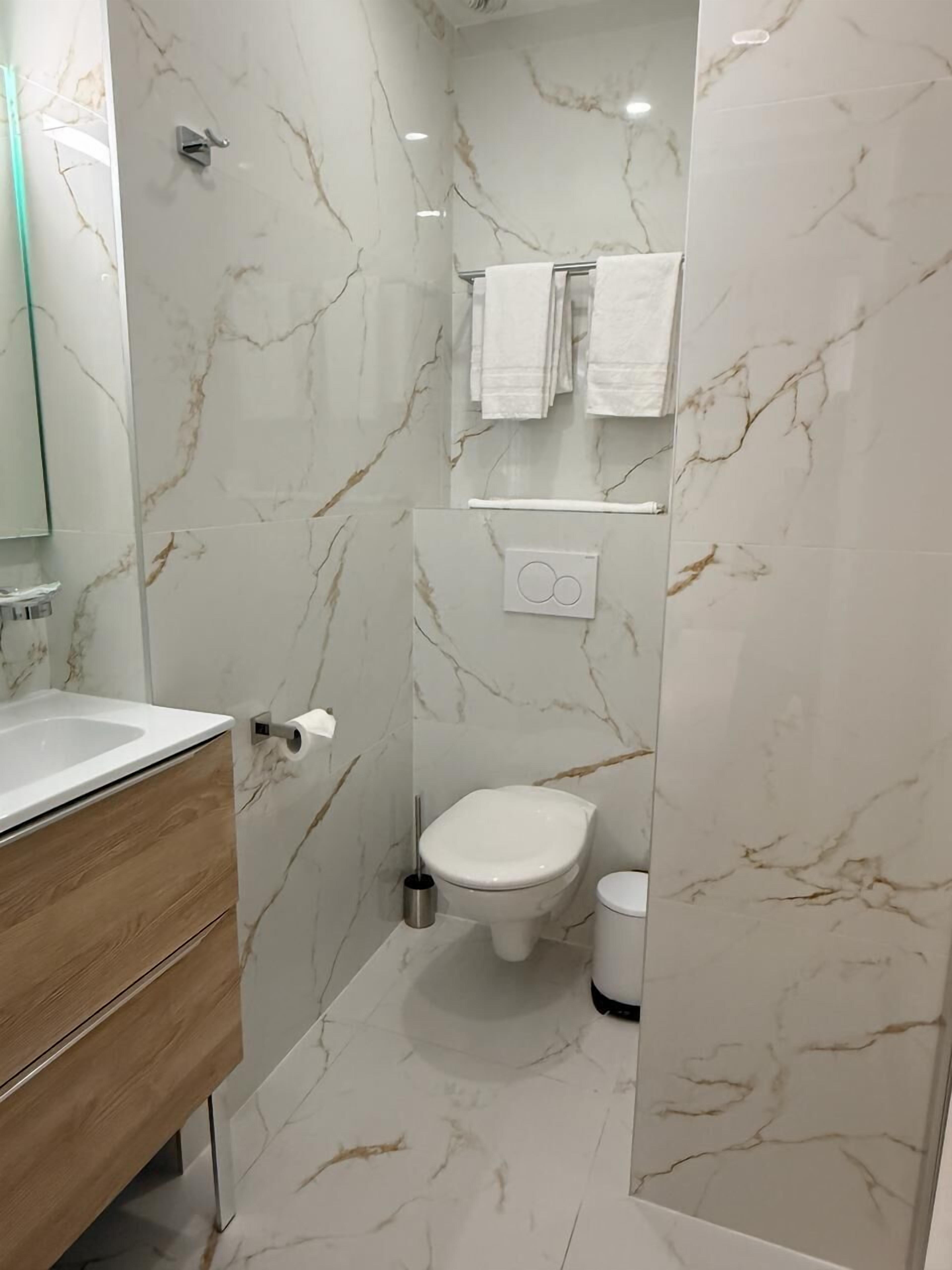 Un baño moderno con salpicadero de mármol, tocador de madera, inodoro y barra para toallas.
