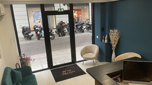 Un espace d’accueil d’hôtel au design moderne, comprenant un comptoir d’accueil, un espace d’attente avec un canapé et une vue sur les motos garées à l’extérieur.
