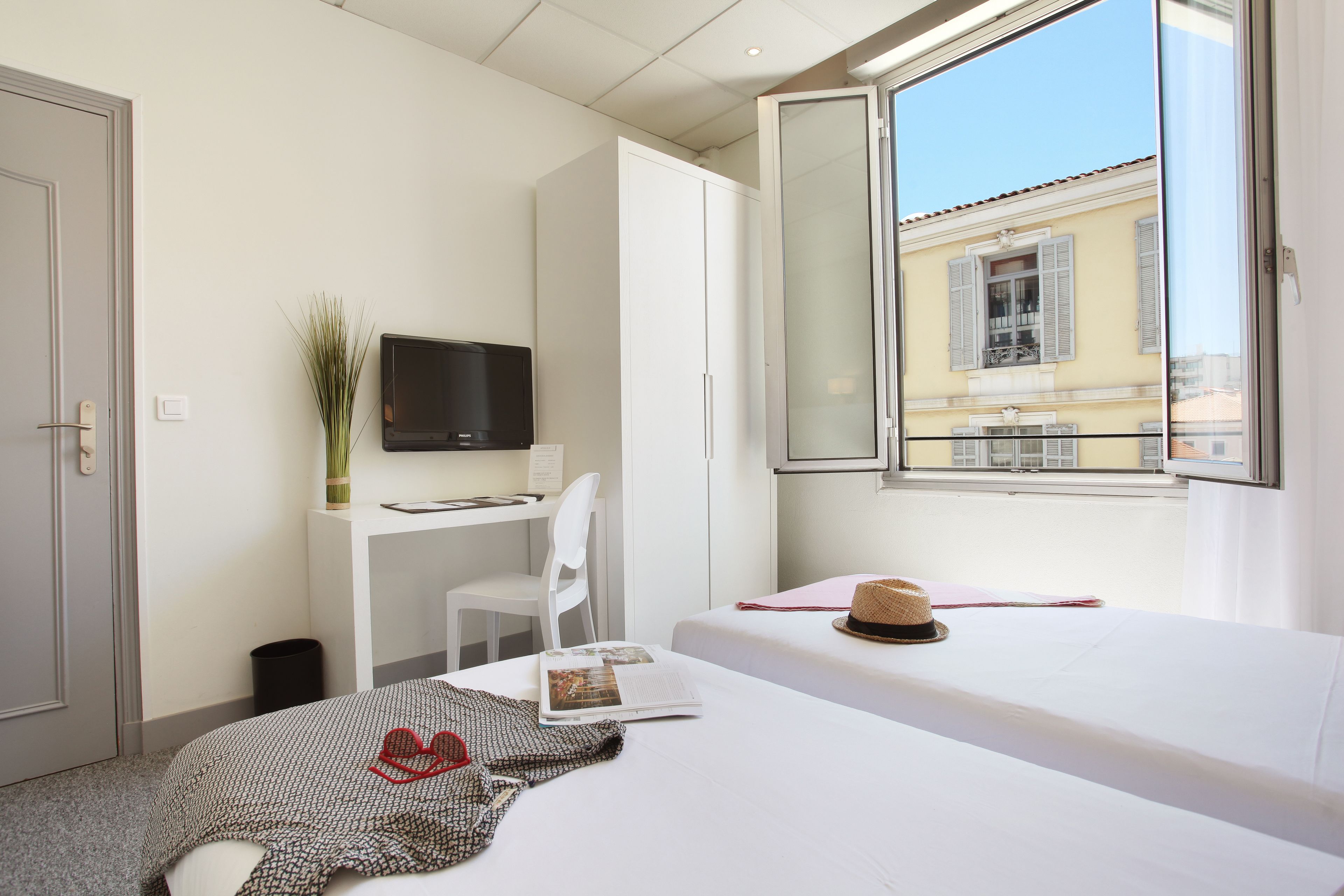 A hotel room with a bed, a desk, a chair, a TV, and a window with a view of buildings.
