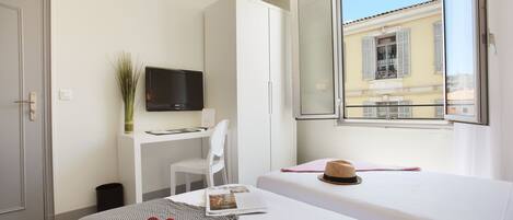 A hotel room with a bed, a desk, a chair, a TV, and a window with a view of buildings.