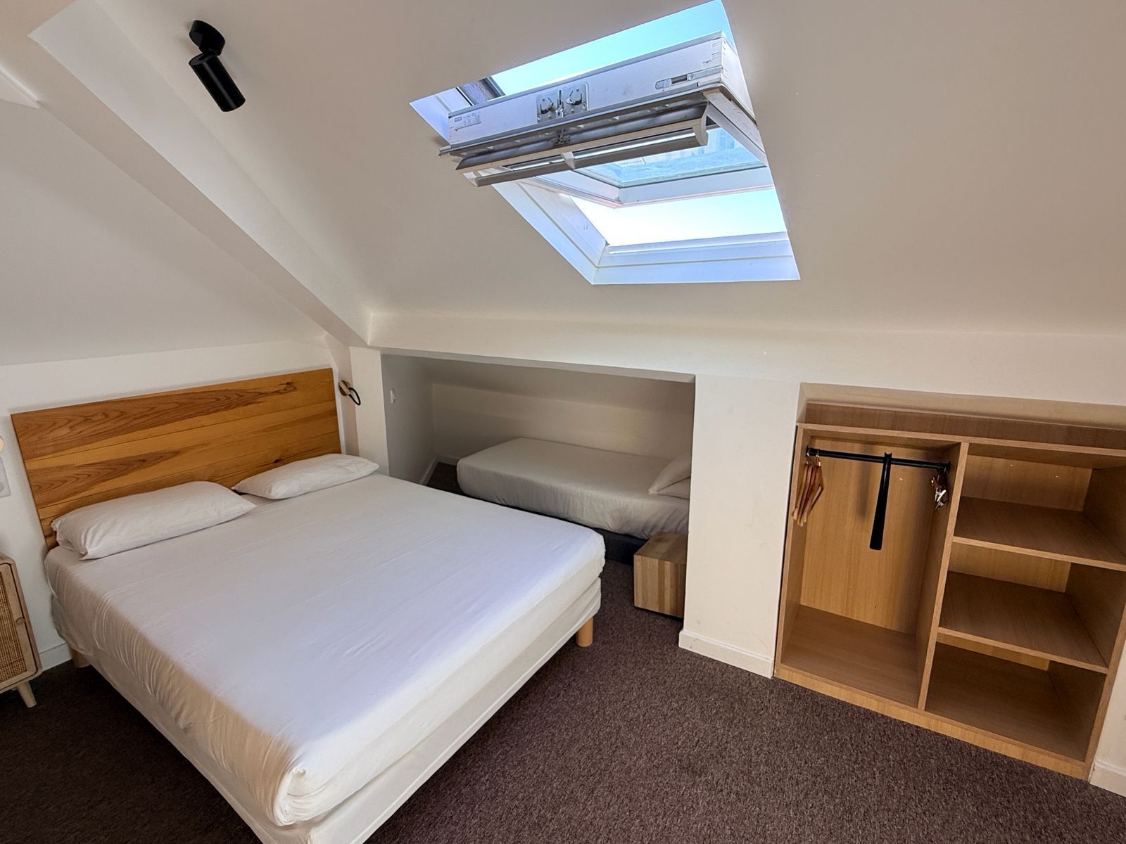 A compact room with a skylight, a bed, a wardrobe, and a small seating area.