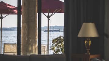 A view from a window with a lamp on a side table, a red umbrella, and a distant boat on the water.