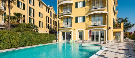 A hotel with a swimming pool, multiple balconies, and a well-maintained garden.