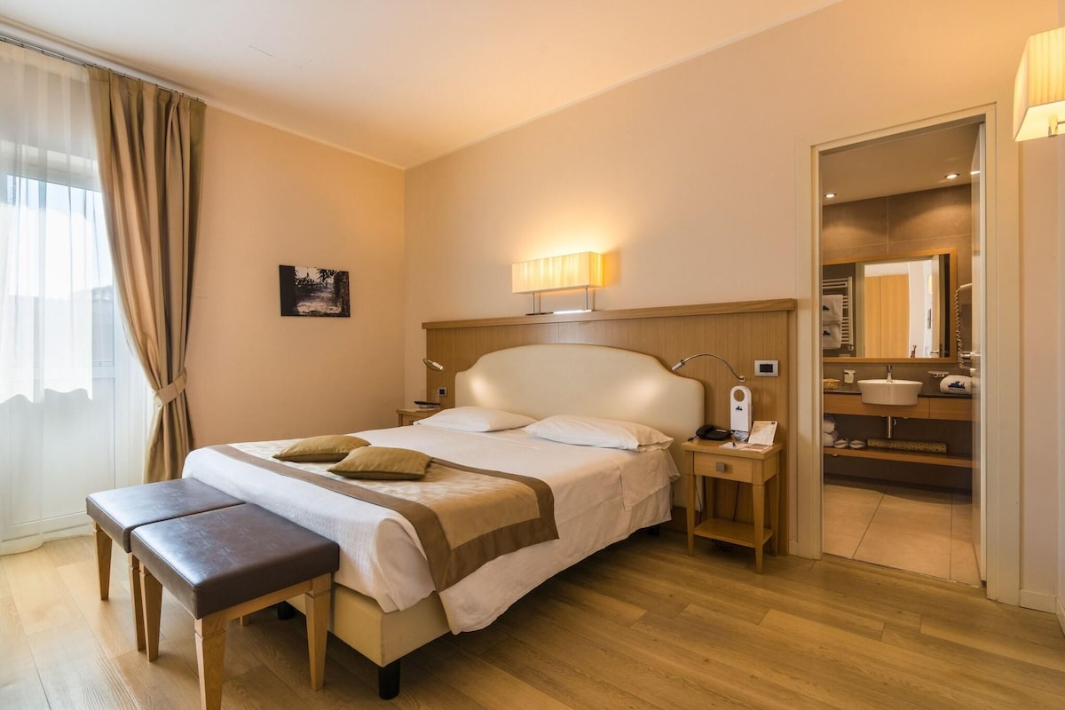 Ein Hotelzimmer mit Bett, Nachttisch, Lampe und einer Bank.