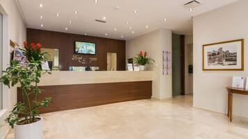 A hotel reception desk with a wooden counter, a television screen, and a framed picture on the wall.