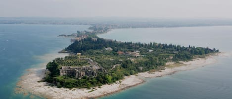 An aerial view of a coastal island with a historic building surrounded by greenery and a clear view of the sea.
