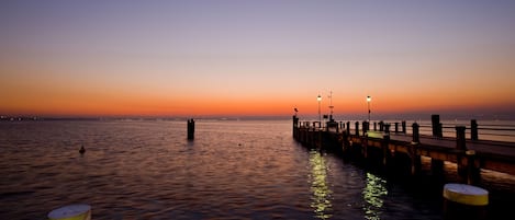 Une jetée s’avançant dans une étendue d’eau calme au coucher du soleil, avec des lampadaires disposés le long de sa longueur.