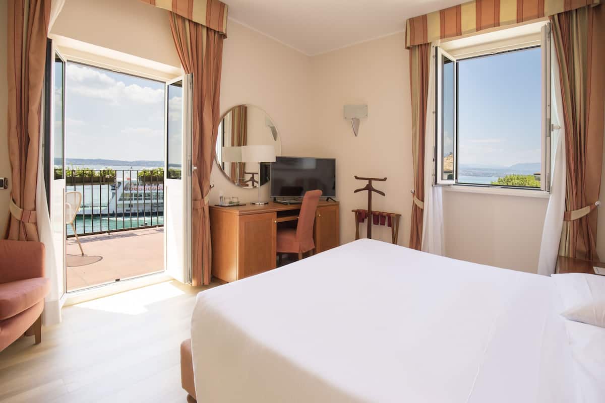A hotel room with a bed, desk, chair, TV, and a balcony with a view.