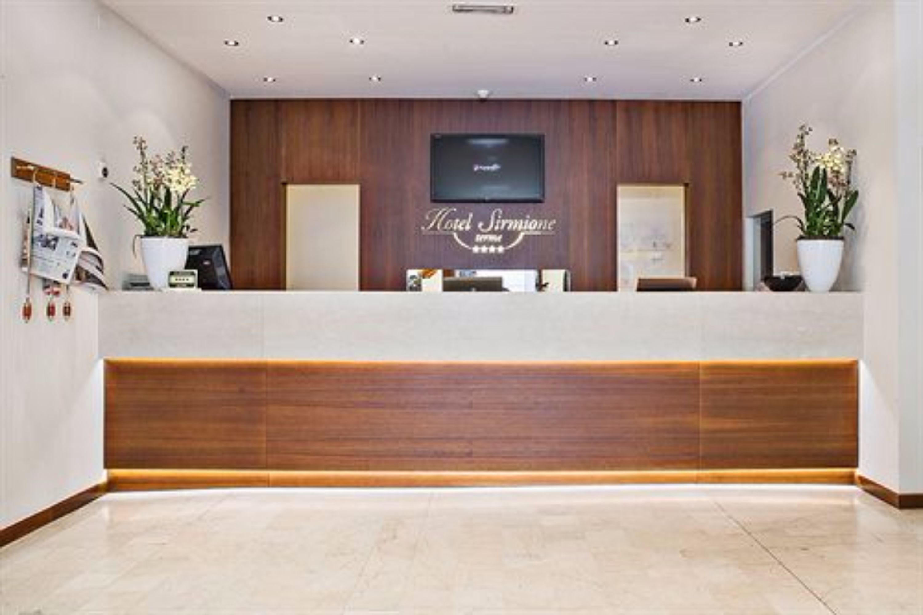 Un mostrador de recepción de hotel con un panel de madera de fondo, un televisor de pantalla plana y plantas en macetas.