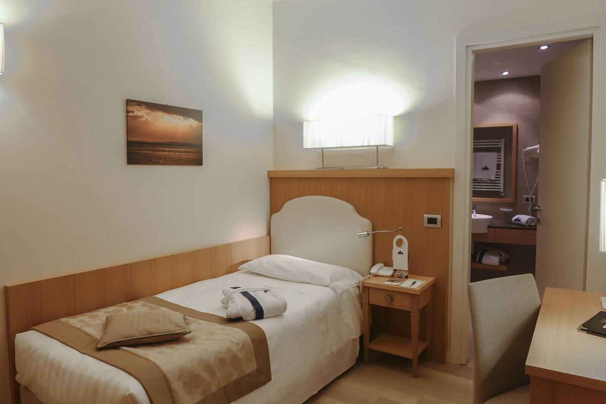 A hotel room with a bed, bedside table, chair, and a painting on the wall.