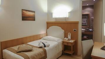 A hotel room with a bed, bedside table, chair, and a painting on the wall.