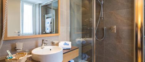 A modern bathroom with a glass-enclosed shower, a large mirror, and a wooden vanity with a sink and towel rack.