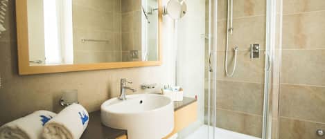 Un baño con lavamanos, espejo, toallero y ducha.