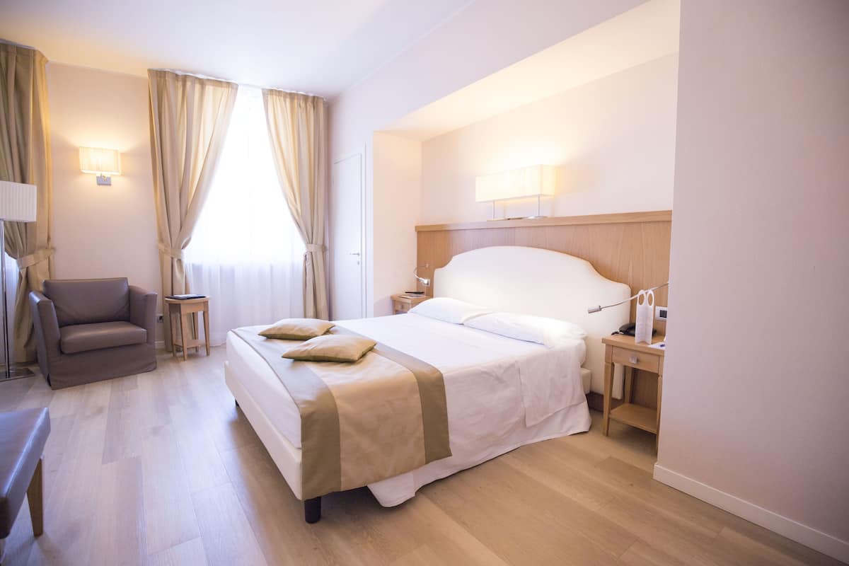 A hotel room with a large bed, bedside tables, a chair, and a lamp.