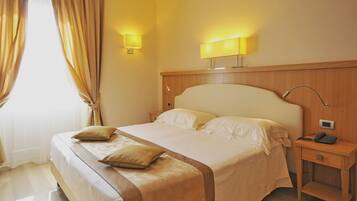 A hotel room with a large bed, two bedside lamps, a nightstand with a phone, and curtains on the window.