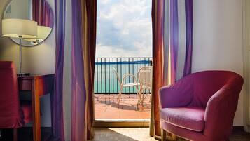 Una habitación con vista al mar, un espejo redondo, un sillón morado y piso de madera.
