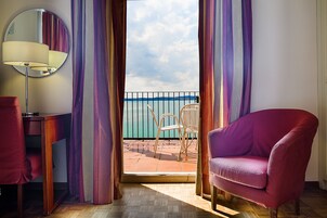 A room with a view of the sea, a round mirror, a purple armchair, and a wooden floor.