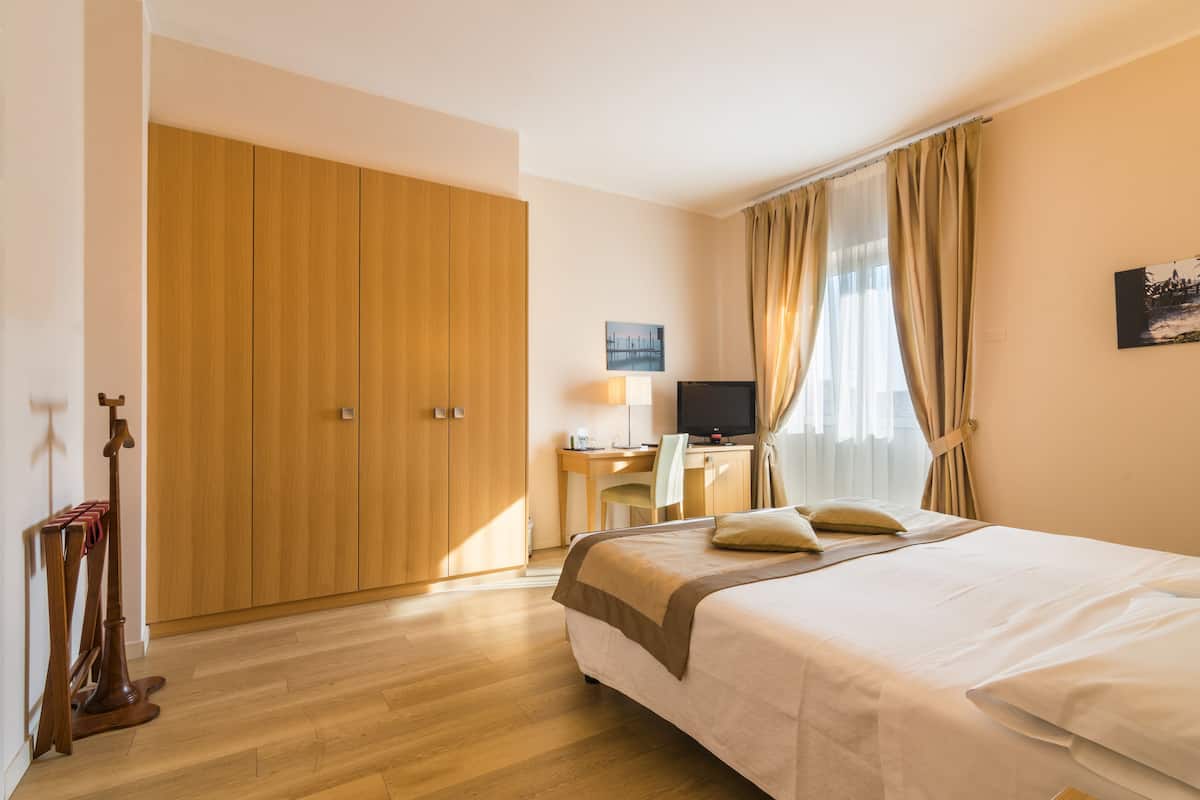 A hotel room with a bed, a desk with a computer, a TV, and a wardrobe.