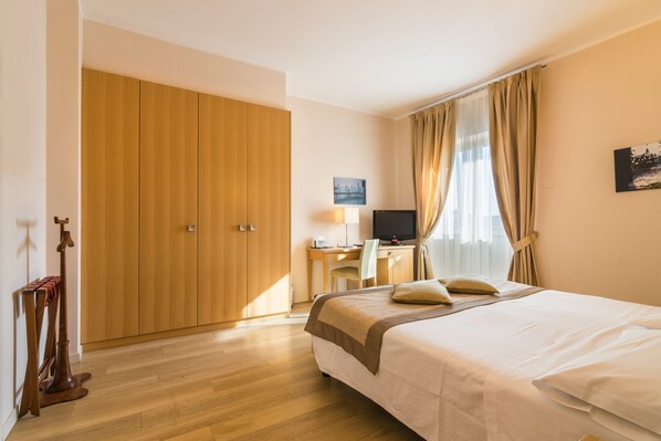 A hotel room with a bed, a desk with a computer, a TV, and a wardrobe.
